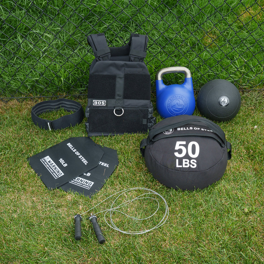 The Bells of Steel USA Ultimate Backyard Training Bundle features a weighted vest, blue kettlebell, black medicine ball, weightlifting belt, two steel plates, a 50 lbs sandbag, and a jump rope—all the equipment you need for the ultimate outdoor workout or backyard gym.