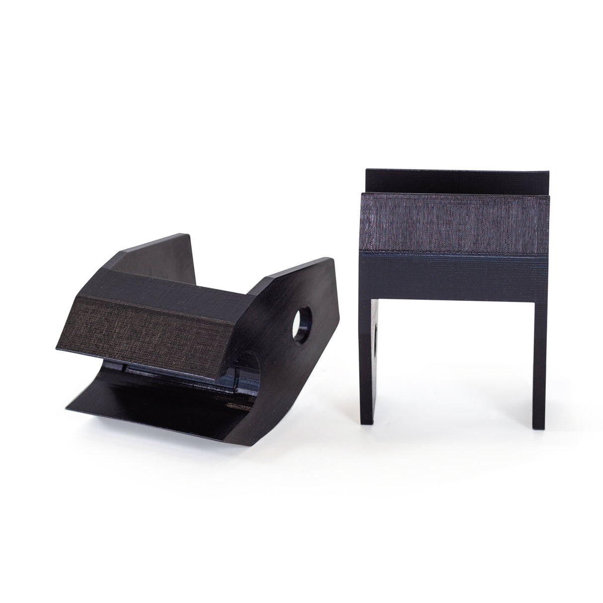 Two black, angular plastic Above Rack Barbell Holders by Bells of Steel are shown against a white background: one lies at an angle displaying a side hole, while the other stands upright on two legs.