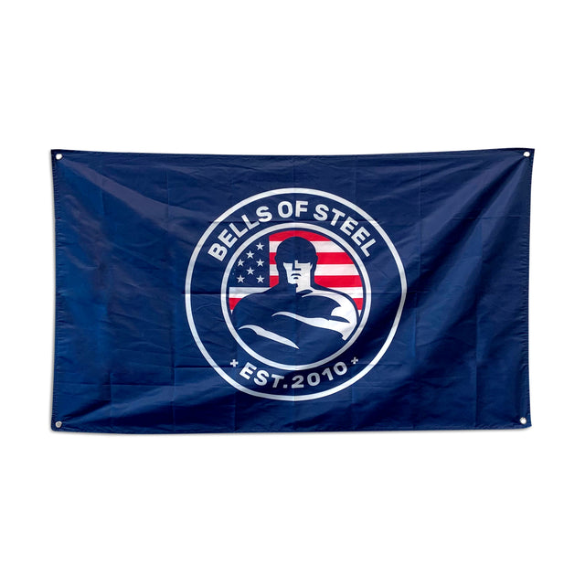 A blue gym flag features a muscular figure logo with an American flag backdrop and the text "Bells of Steel" and "Est. 2010" in a circular border, ideal for home gym decor.