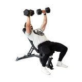 A man uses the Bells of Steel Adjustable Utility Bench to perform an incline bench press with dumbbells, dressed in a gray t-shirt, black pants, and white shoes. He lifts above his chest for upper body strength, varying incline angles to test maximum capacity.