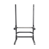 A picture of a 3"x3" black power rack features adjustable barbell holes and a rectangular base to ensure stability, complemented by the utility seat from Bells of Steel's Hydra/Manticore line for performing squats and presses in strength training.