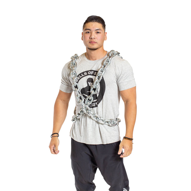 A man models the Bells of Steel Chain Weight Vest over a gray graphic t-shirt and black pants, standing against a white background to showcase this strength training accessory.