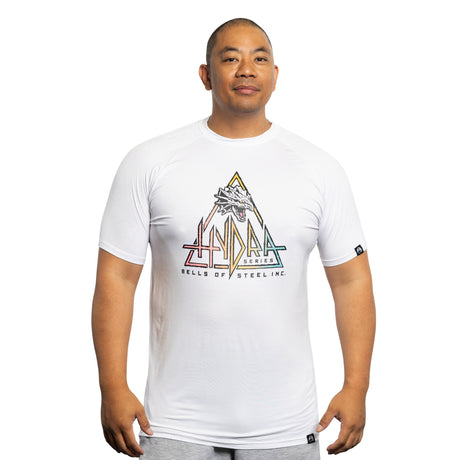 A man wears the Bells of Steel Bamboo T-Shirt, featuring a colorful triangle graphic and "HYDRA SERIES BELLS OF STEEL INC." text, while standing against a white background and looking slightly to the side with a neutral expression.