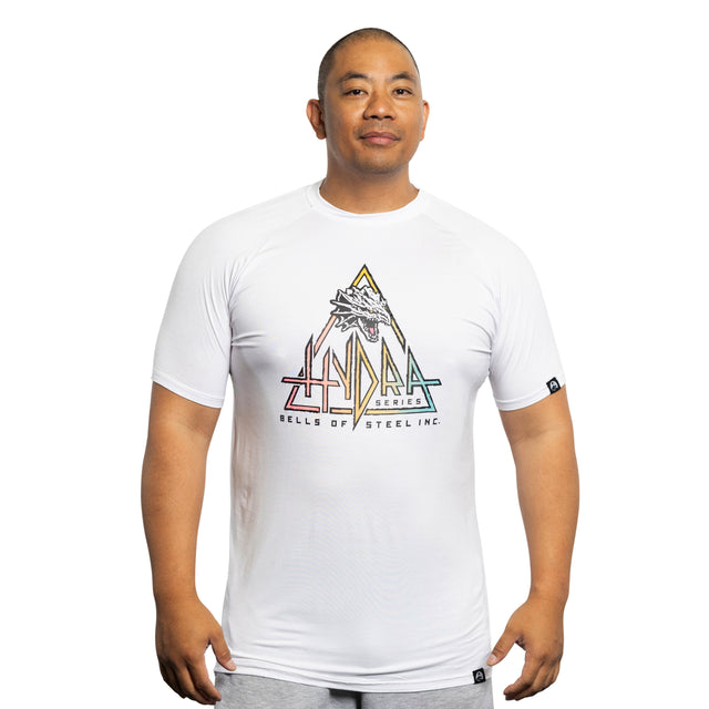 Against a plain white backdrop, someone models a Bells of Steel Bamboo T-Shirt, showcasing buttery softness and adorned with a colorful geometric pattern featuring a Hydra and mountain design, emphasizing sustainability.