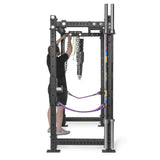 A person in athletic wear adjusts lifting chains on a black metal rack equipped with the Bells of Steel Accessory Holder (Wall or Rack Mounted), along with purple resistance bands and color-coded barbell collars, viewed from the front.