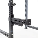 Close-up of the black metal Spotter Arms Rack Attachment by Bells of Steel, featuring adjustable parts with a hole grid for customization. The UHMW lining underscores its sturdy construction and essential role in fitness and weightlifting routines.