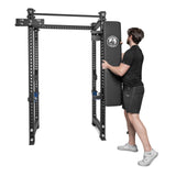 A man in athletic wear mounts the Bells of Steel Wall or Rack Mounted Bench Hanger onto a black metal power rack, efficiently organizing gym space against a plain white background.