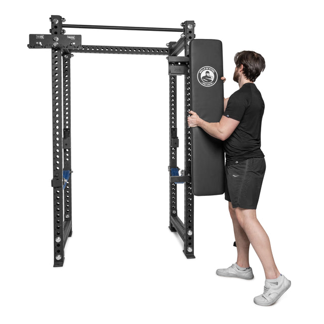 A man in athletic wear mounts the Bells of Steel Wall or Rack Mounted Bench Hanger onto a black metal power rack, efficiently organizing gym space against a plain white background.