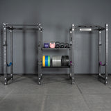 A gym setup featuring two squat racks, a pull-up bar, colorful kettlebells, and a Bells of Steel USA rack with plates—neatly organized with Divider for Bumper Plate Shelf (Pack of 3) against a gray wall and floor with shelving.