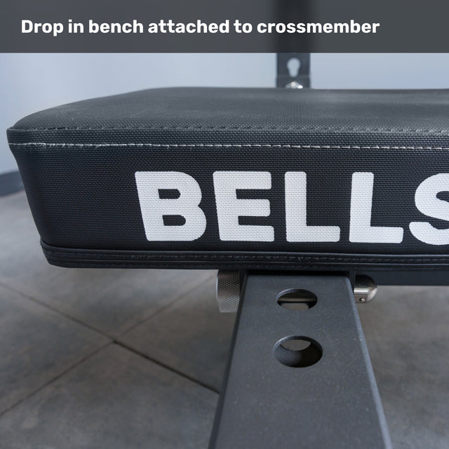 Close-up of a padded gym bench labeled "Bells of Steel USA," attached to the Crossmember For Converter Bench - 43" with adjustment holes; text above reads "Drop in bench attached to crossmember," ideal for two-post rack setup.