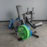 The Bells of Steel USA Legacy Leg Extension / Hamstring Curl Machine – Plate Loaded, featuring black padding and a metal frame with green and blue plates, stands on a gray gym floor—ideal for any home gym setup.