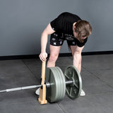 A person in a black shirt and shorts uses a wooden jack to lift a loaded Bells of Steel USA Deadlift Bar off the gym floor, getting ready to adjust the weight plates like in powerlifting.