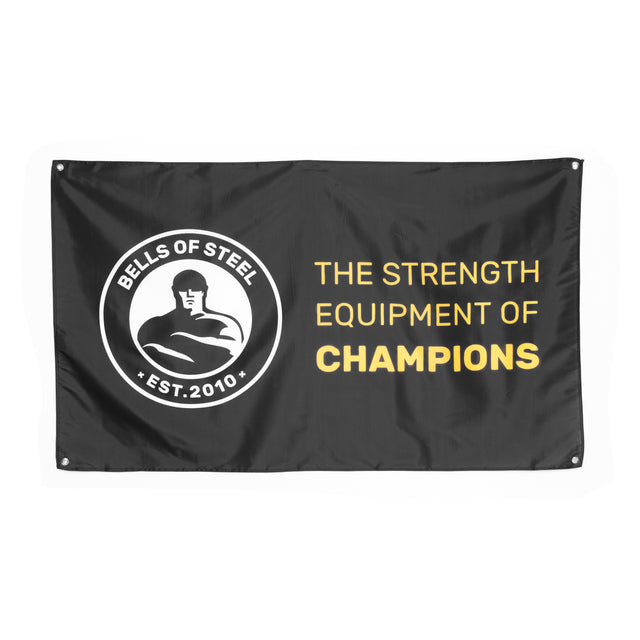 A black Bells of Steel gym flag features a left-side logo with a muscular figure and "BELLS OF STEEL EST. 2010," while the right side boldly states "THE STRENGTH EQUIPMENT OF CHAMPIONS" in yellow and white, perfect for enhancing your home gym decor.