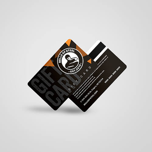 Two overlapping Bells of Steel USA Gift Cards enhance your gainz journey. One card displays the brand logo with bold "Gift Card" text, and the other includes contact info and a magnetic stripe, both featuring sleek black and orange elements.