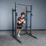 Wearing athletic gear, a person does Nordic hamstring curls inside the Bells of Steel Hydra Half Rack - Prebuilt (3" x 3", ⅝" Holes), using modular components for ankle support—ideal for an efficient home gym.