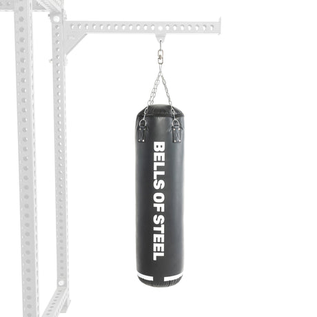 A Bells of Steel Heavy Bag Set is suspended from a metal frame by chains, with the sturdy support, similar to a power rack, partially visible on the left against a white background.