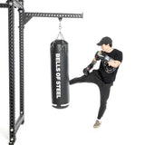 Wearing a black cap, t-shirt, pants, and checkered shoes, an individual skillfully kicks a Bells of Steel Heavy Bag Set while wearing boxing gloves. The black punching bag hangs securely from a sturdy mounting solution.