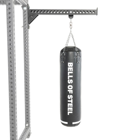 A black heavy bag from Bells of Steel USA hangs from a chain attached to a sturdy metal support frame, making this Heavy Bag Set an ideal addition to any power rack or gym setup, displayed against a white background.