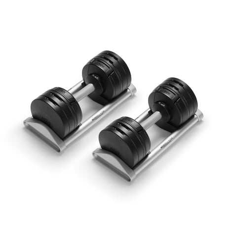 The Bells of Steel USA NÜOBELL-S Adjustable Dumbbells feature metal handles and rest on a silver stand. Ideal for home gyms, these round weights adjust to various resistance levels for versatile workouts.