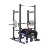 A person dressed in black performs a bench press under a barbell with weights on the sturdy Hydra Half Rack - Prebuilt by Bells of Steel. The modular weightlifting rack features 3" x 3" dimensions with ⅝" holes, set against a white background.