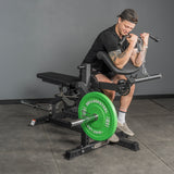 A man performs preacher curls with a chain attachment on a weight machine in a gym. A green 25 lbs plate is beside the Bells of Steel USA Legacy Leg Extension / Hamstring Curl Machine - Plate Loaded.