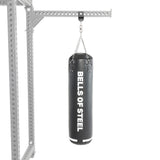 A heavy black punching bag hangs from a metal frame using the Bells of Steel Utility Shackle Rack Attachment by chains, highlighting reliable gym equipment mounting against a plain white background.
