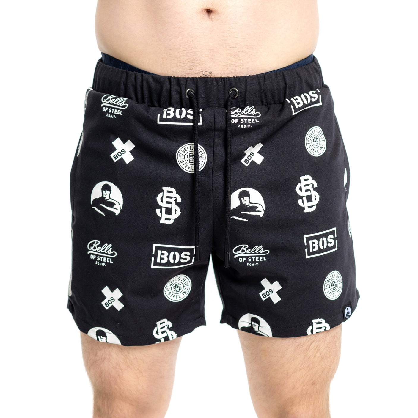 A person wearing Bells of Steel Gym Shorts in black, made from stretchy lightweight fabric and featuring white "Bells of Steel" and "BOS" logos, stands against a plain white background.