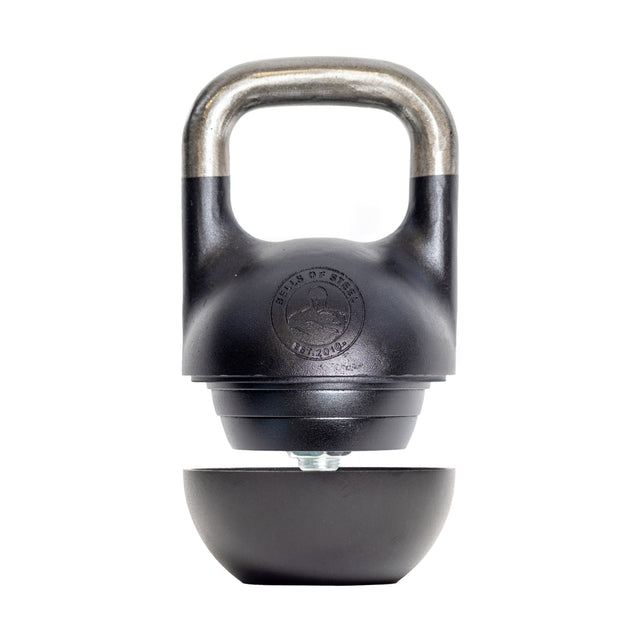 Introducing the Mark Wildman Adjustable Kettlebell by Bells of Steel, featuring a sleek silver handle and black body with our logo. This modular marvel includes a detachable bottom weight plate, offering versatile workout options while resting open below when not in use.